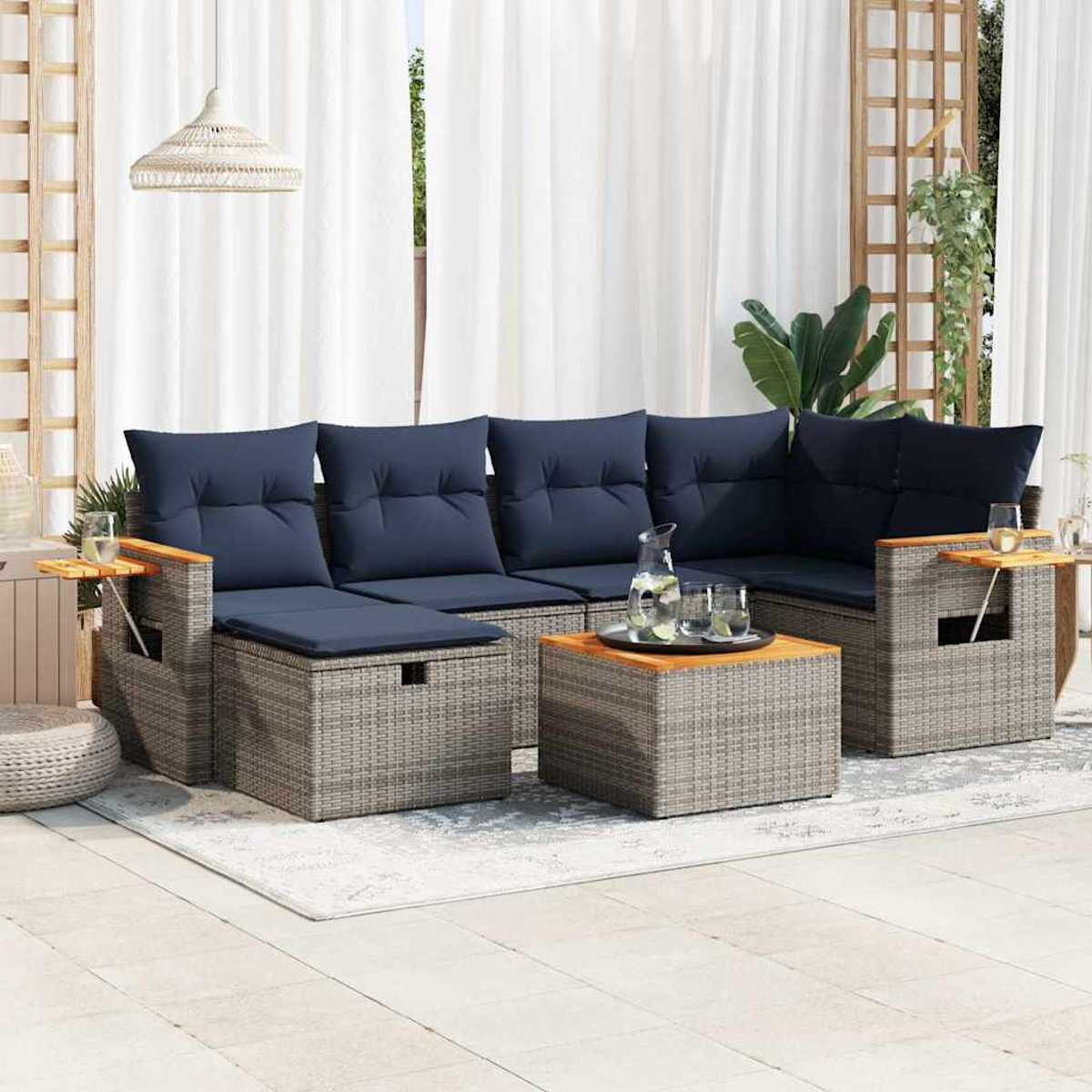 Rattan-Sofagarnitur mit blauen Kissen, einem quadratischen Tisch und einem Beistelltisch. Es liegt auf einem Teppich.