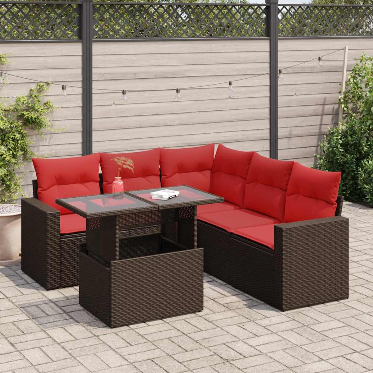 Braunes Korbsessel-Set mit roten Kissen, Hubtisch und Pflanzen im Hintergrund.