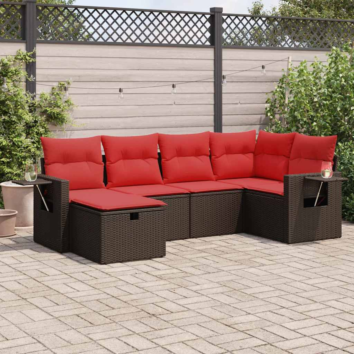 Gartensofa mit roten Kissen auf einer Ziegelterrasse. Ein kleiner Beistelltisch und Pflanzen im Hintergrund.