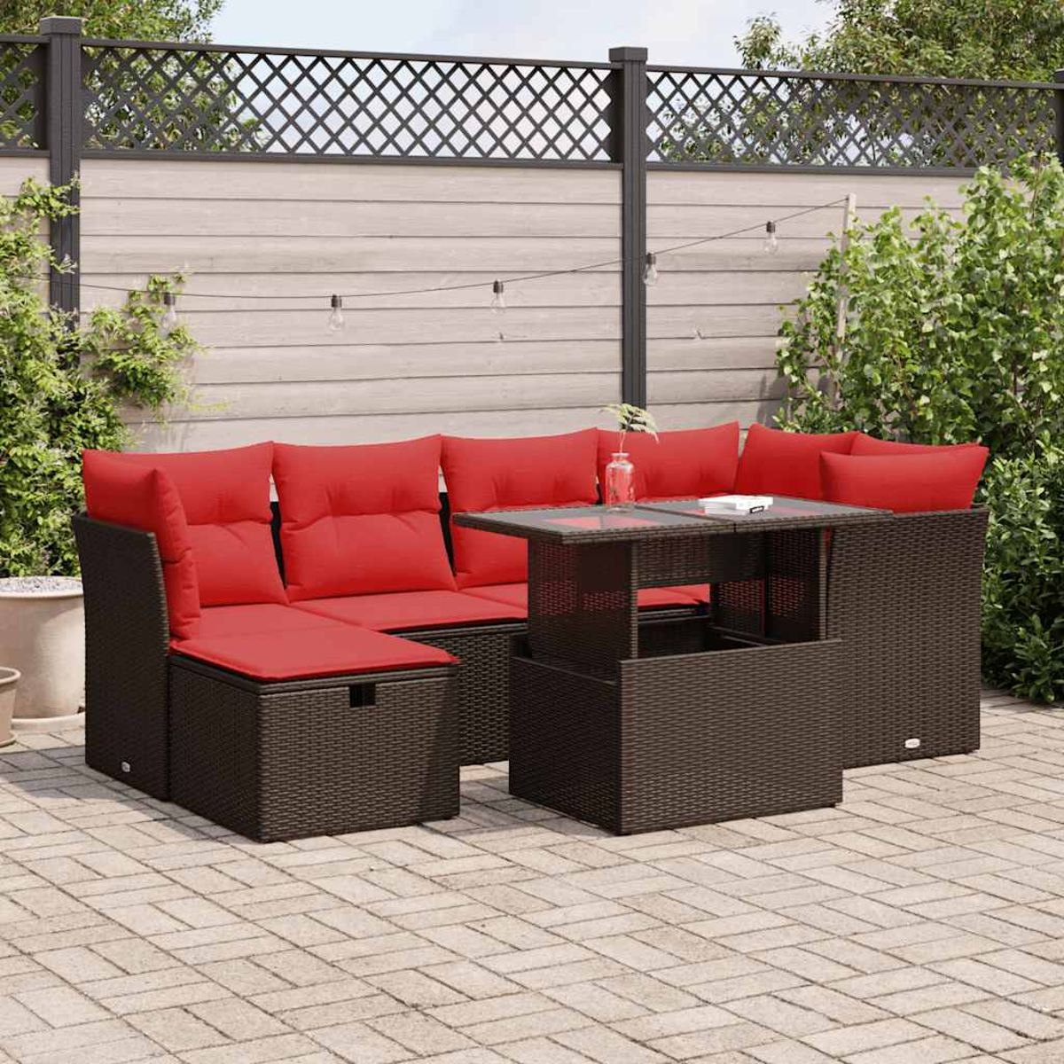 Ein braunes Korbmöbel-Sofa mit roten Kissen und einem Tisch mit Hubfunktion. Draußen.