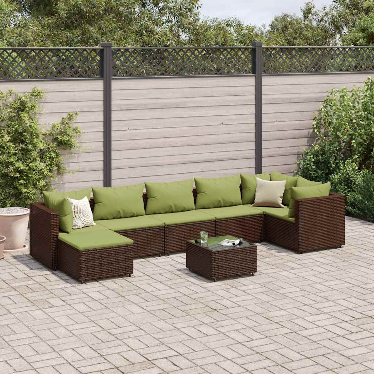 Braunes Rattan-Outdoor-Ecksofa mit grünen Kissen, ein Couchtisch mit Glasplatte auf einer gepflasterten Terrasse.