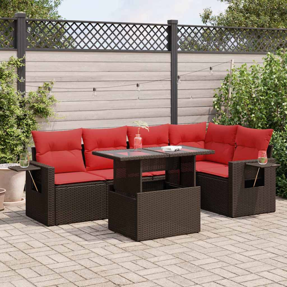 Gartenmöbel-Set mit braunem Rattan-Sofa und Tisch, roten Kissen und Gartenhintergrund.