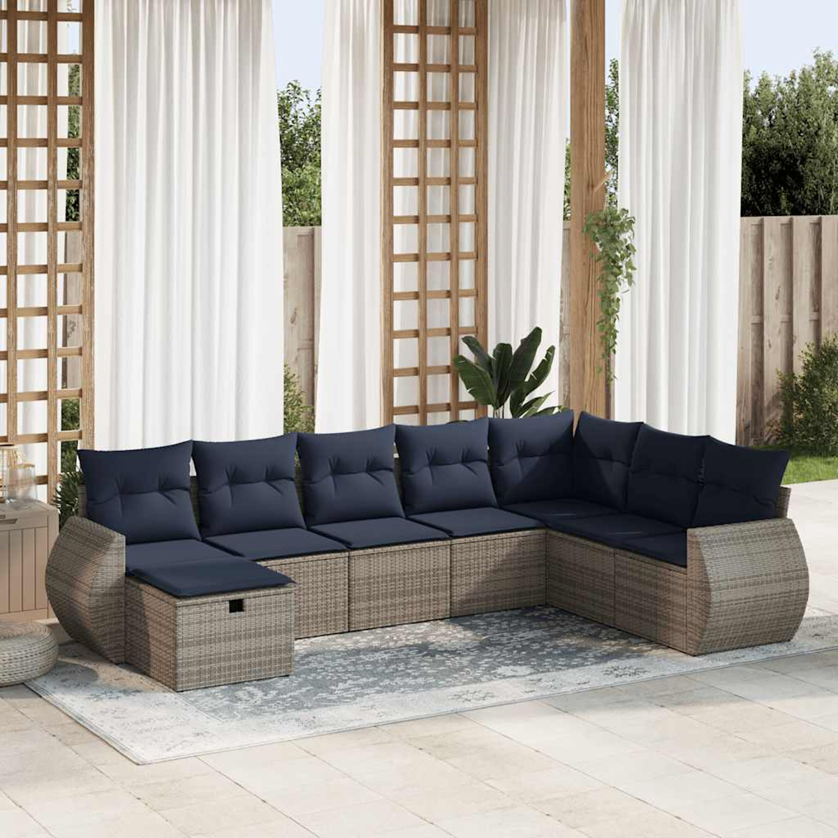L-förmiges Korbmöbel mit blauen Kissen auf einer Terrasse. Weiße Vorhänge und Grün im Hintergrund.