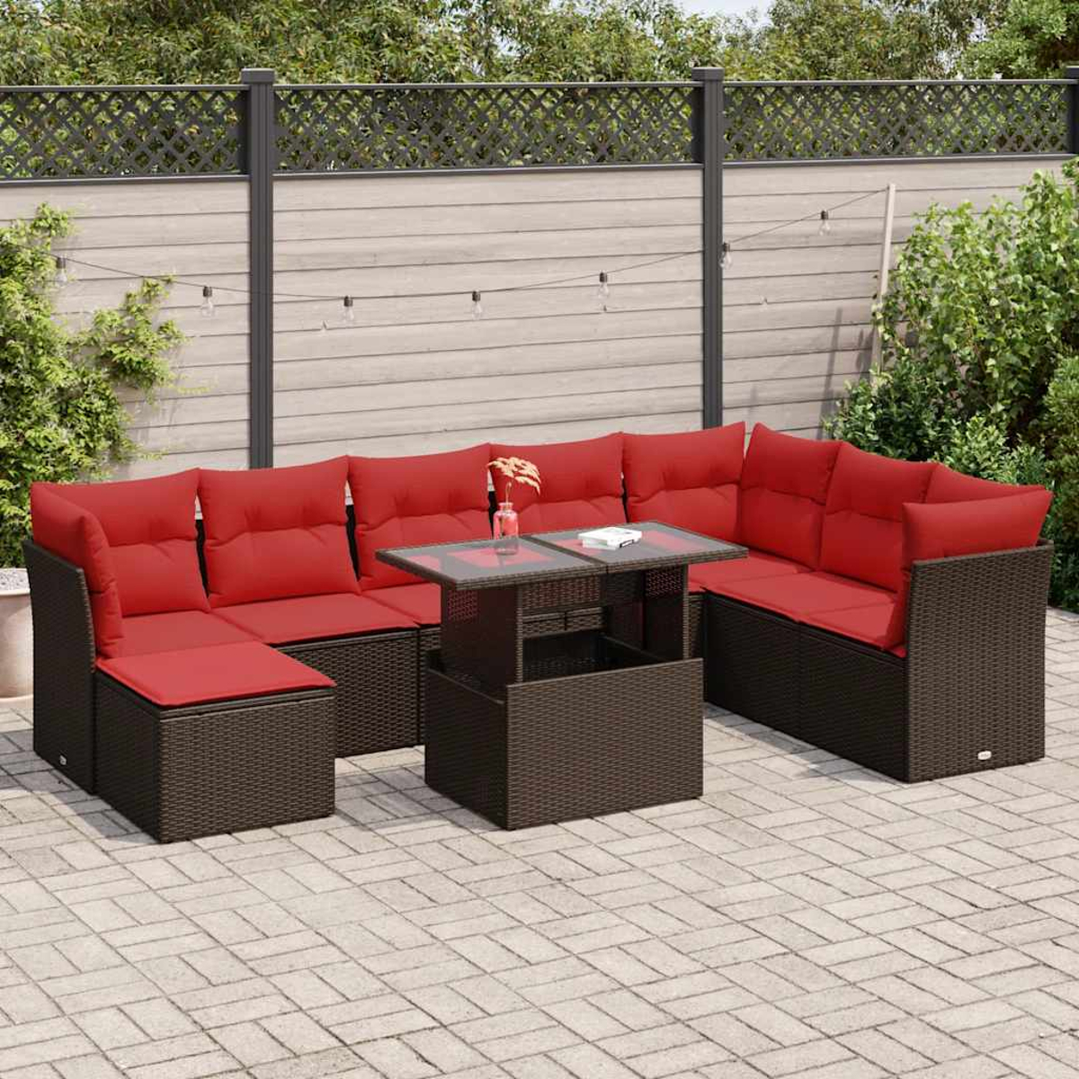 Braunes Ecksofa aus Rattan mit roten Kissen und einem Couchtisch mit Hebefunktion. Terrasse mit Pflanzen.
