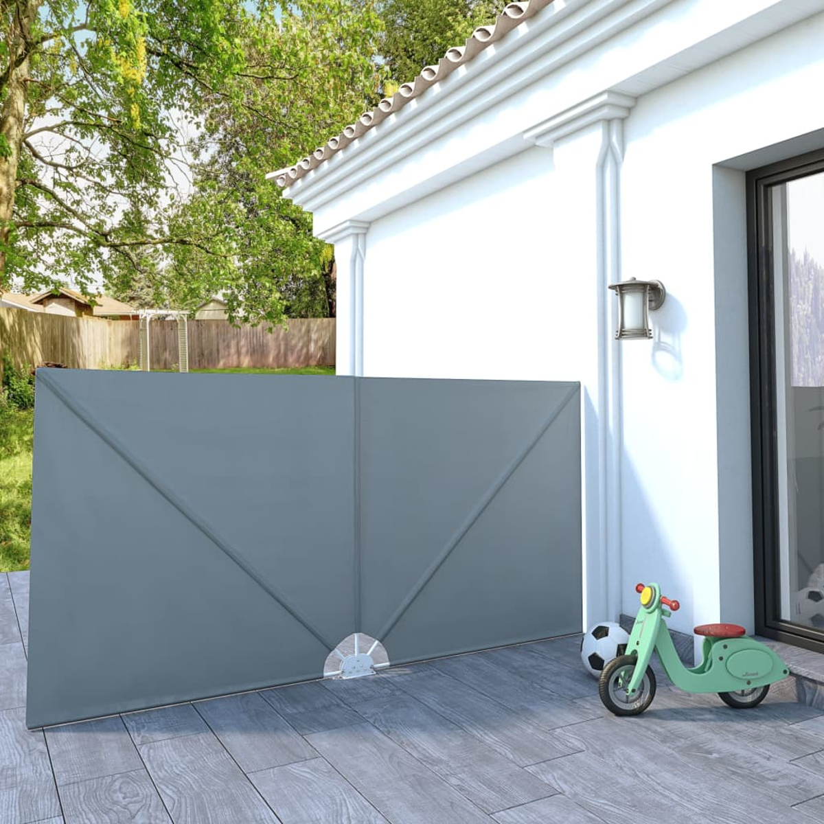 Ein grauer Sichtschutz vor einem Haus, mit einem Spielzeugmotorrad und Ball daneben.