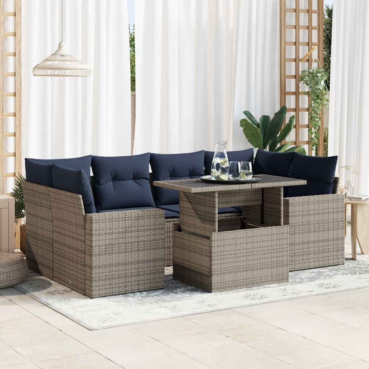 Ecksofa aus grauem Weidengeflecht im Freien mit blauen Kissen, einem Tisch mit Hubplatte und weißem Vorhanghintergrund.
