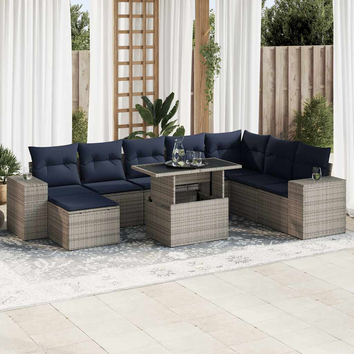 Ecksofa aus grauem Weidengeflecht im Freien mit blauen Kissen, einem Tisch mit Hubplatte und Glaswaren.
