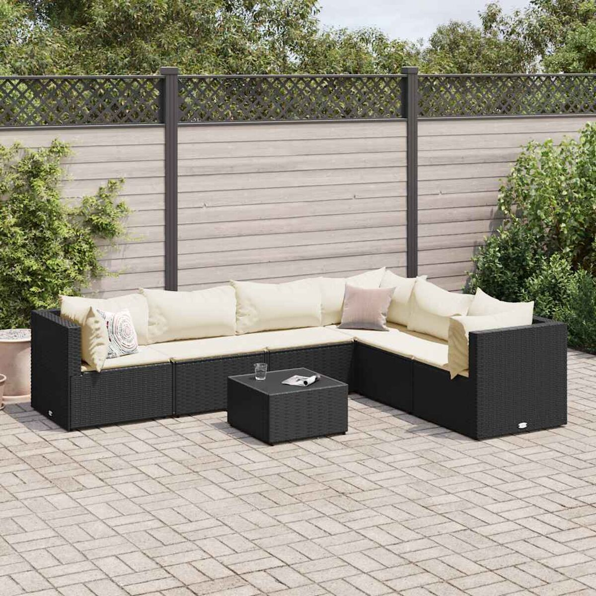 Schwarzes Ecksofa aus Weide mit cremefarbenen Kissen und einem quadratischen Couchtisch auf einer Ziegelterrasse.