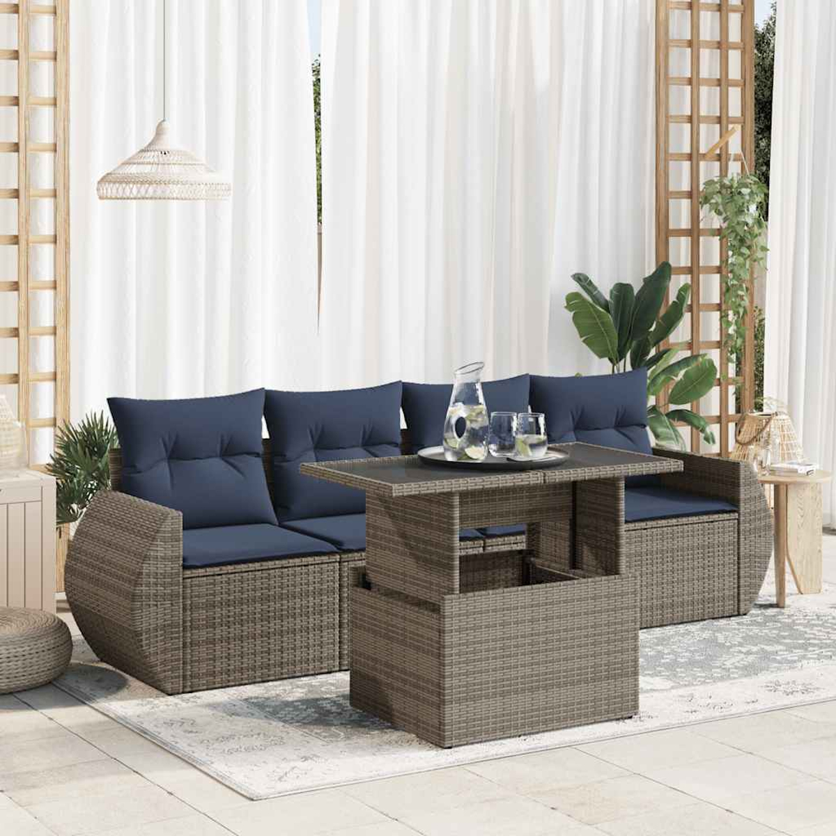 Graues Outdoor-Sofa aus Korbgeflecht mit blauen Kissen, Tisch und weißem Vorhang im Hintergrund.