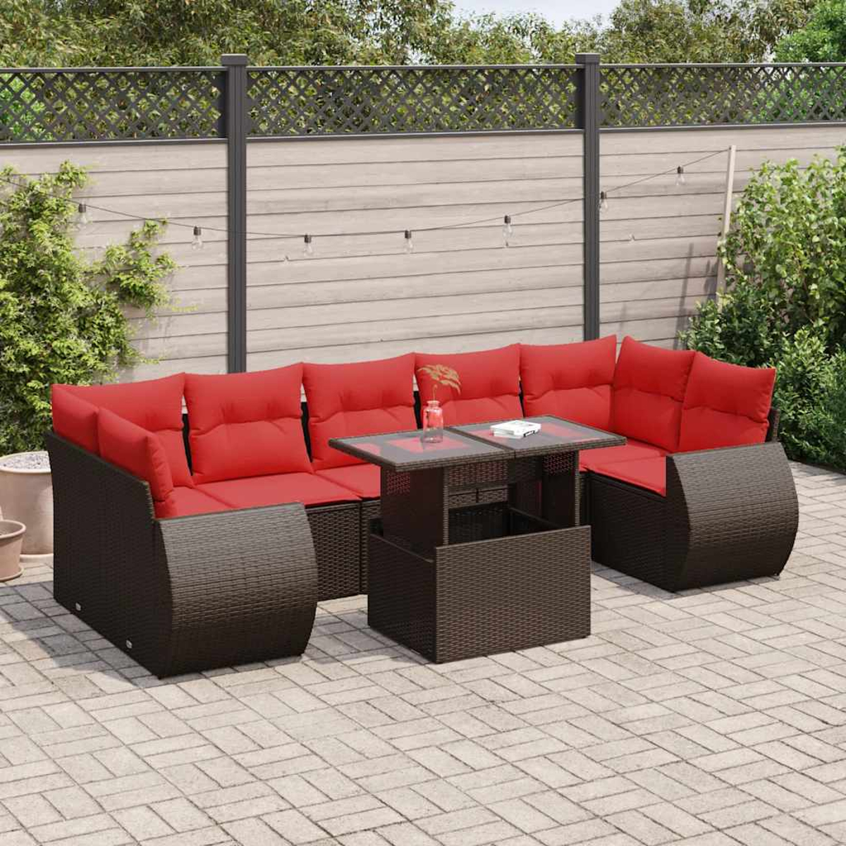 Sofá seccional exterior de mimbre marrón con cojines rojos y mesa de cristal.