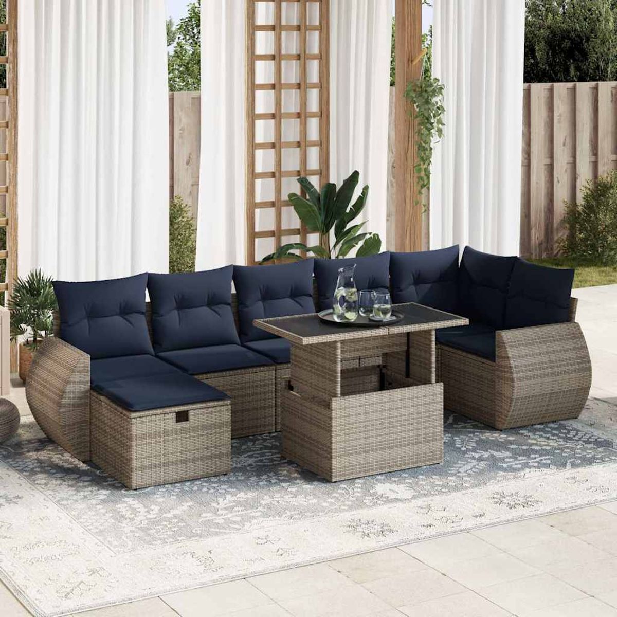 Outdoor-Wicker-Sofagarnitur mit blauen Kissen, Tisch und Teppich. Vorhänge und Grün im Hintergrund.