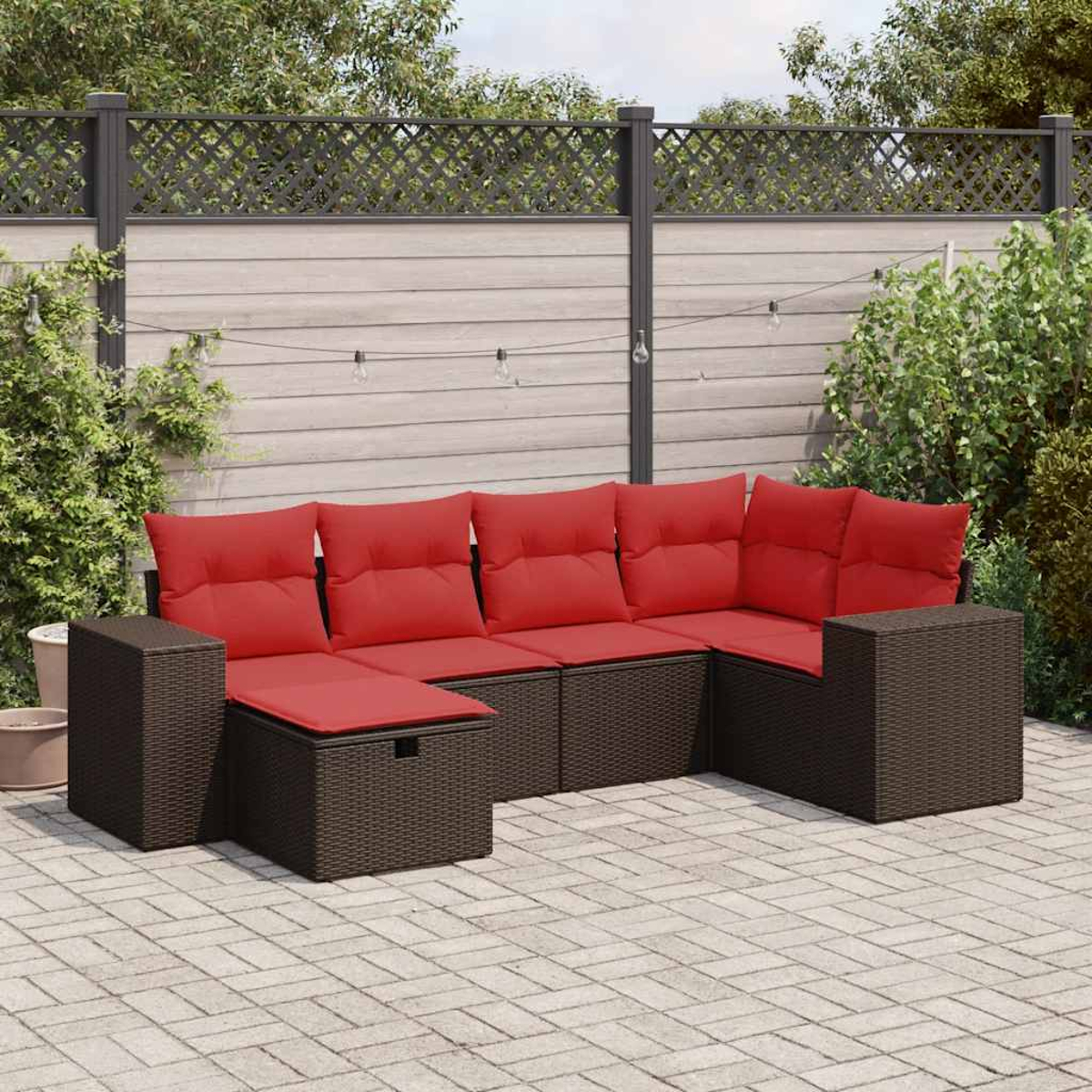 Braunes Ecksofa aus Korbgeflecht mit roten Kissen. Das Set steht auf einer Terrasse. Im Hintergrund sind Zäune und Bäume.