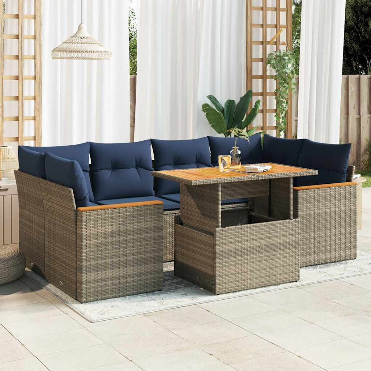 Seccional de ratán para exteriores con mesa elevable. Cojines azules, en patio. Cortinas blancas.