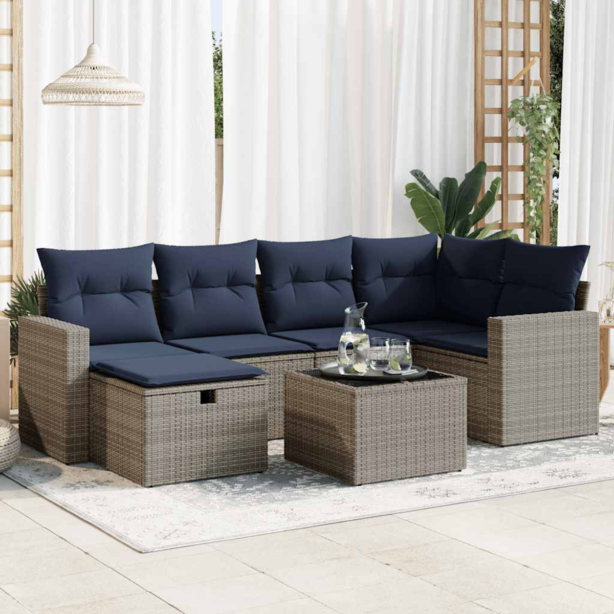 Terrassenset mit Sofa, Tisch und Beistelltisch. Weiße Vorhänge und Pflanzen im Hintergrund.