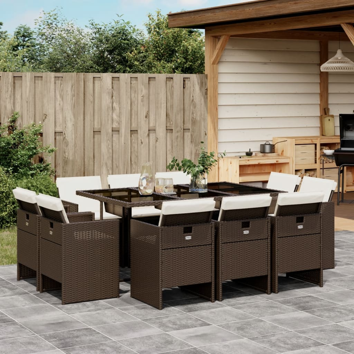 Ein dunkelbraunes Ess-Set aus Korbgeflecht mit cremefarbenen Kissen. Das Set steht auf einer Terrasse mit Außenküche.
