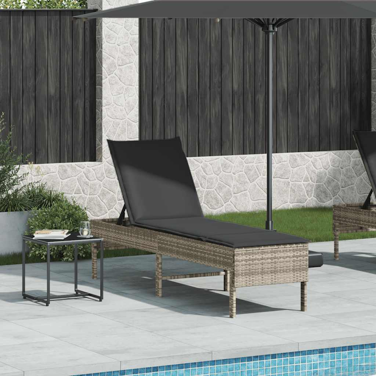 Außenszene mit Rattan-Liegestuhl, Beistelltisch und Sonnenschirm auf einer Terrasse. Hintergrund: Steinmauer und Holzzaun.