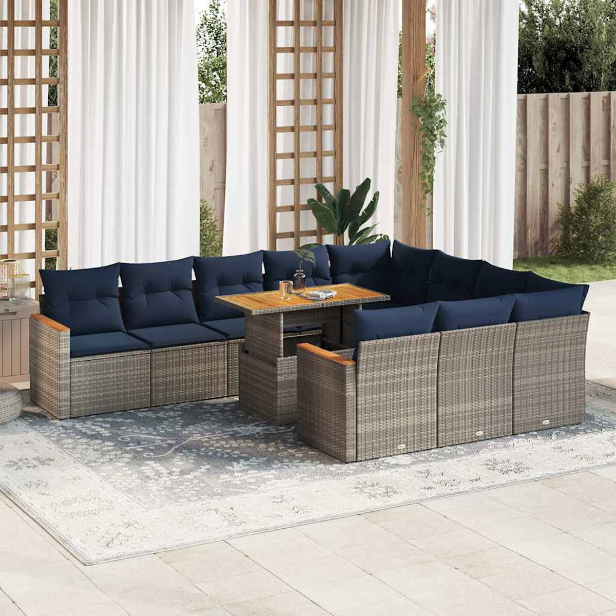 Rattan-Garnitur für draußen mit blauen Kissen, Tisch und Teppich. Transparente Vorhänge und Pflanzen.