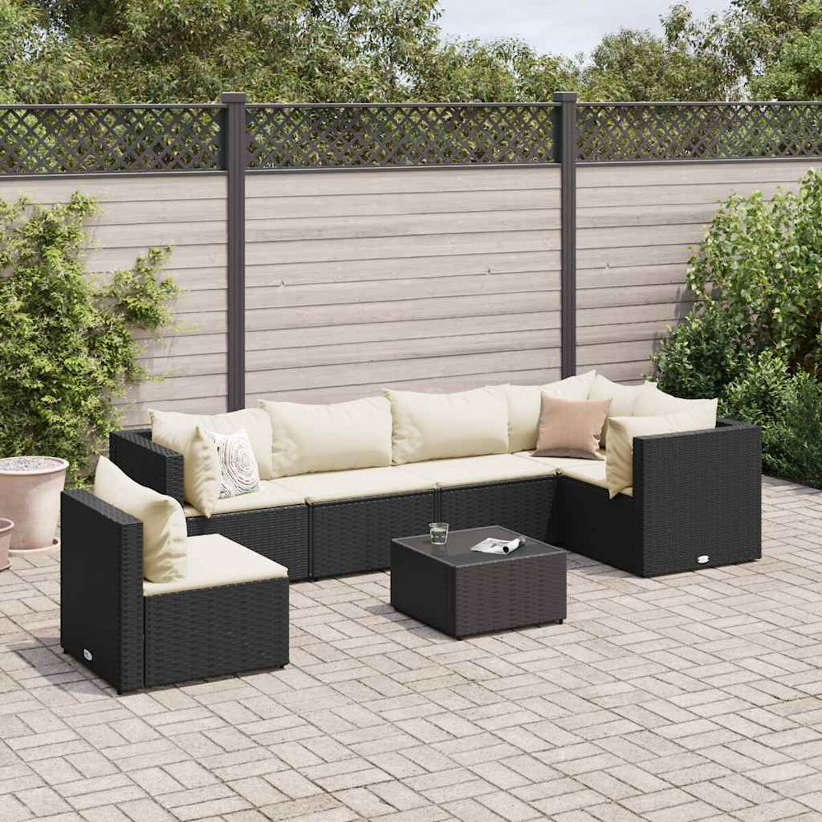 Outdoor-Sitzarrangement mit schwarzem Sofa, cremefarbenen Kissen und einem quadratischen Tisch. Es ist draußen.