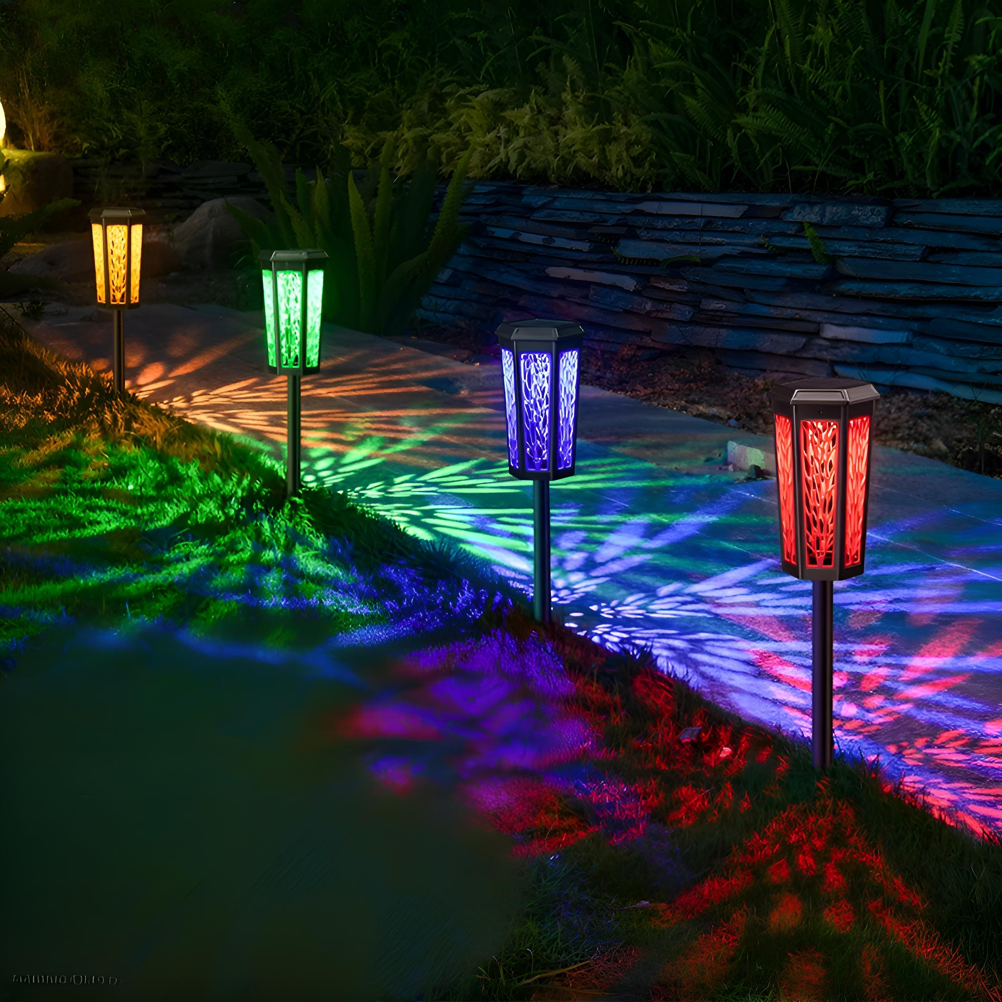 Vier Solar-Gartenleuchten, die Gras beleuchten. Die Lichter haben verschiedene Farben. Der Hintergrund ist ein Steinweg.