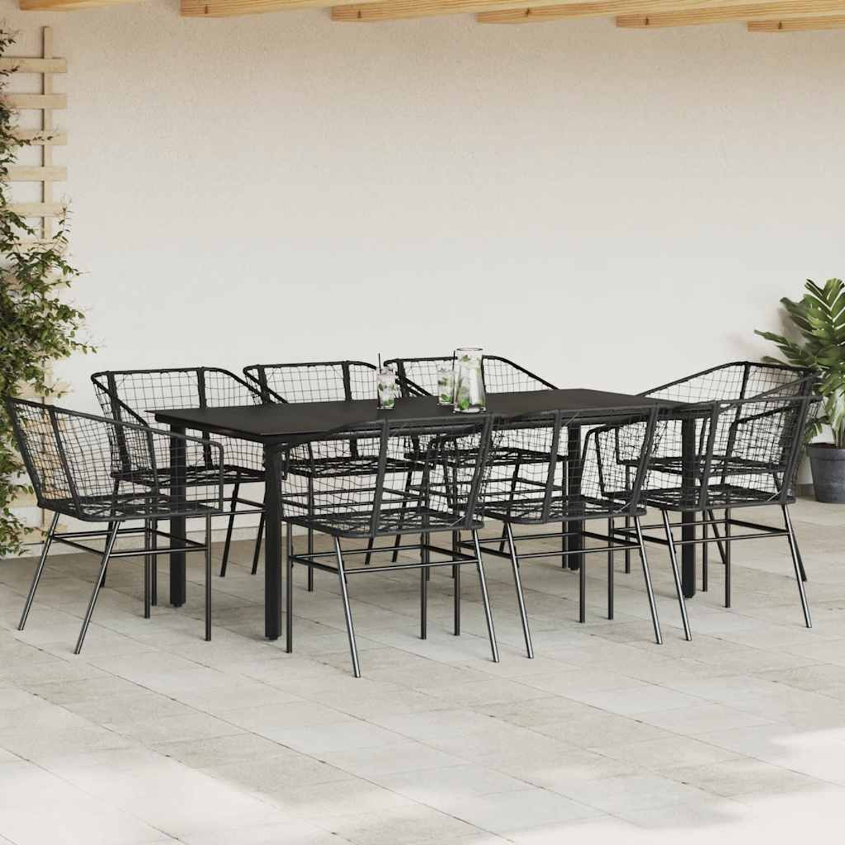 Ein Esszimmer-Set im Freien mit einem schwarzen Tisch und schwarzen Netzstühlen auf einer Terrasse. Es gibt eine Wand und eine Pflanze.