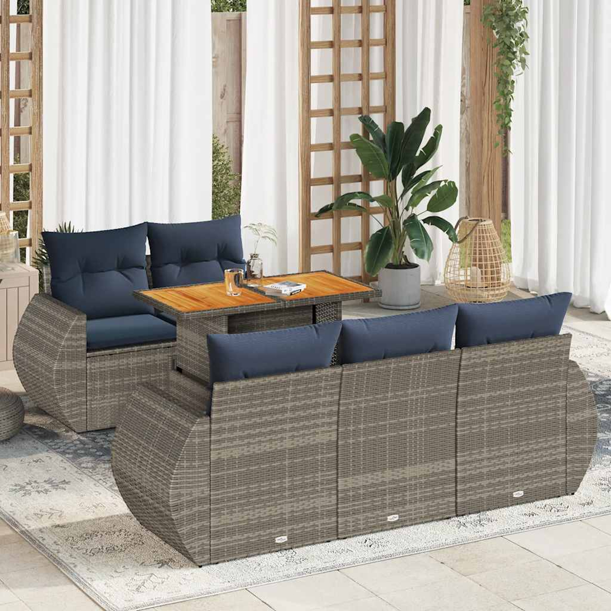 Geflochtene Gartenmöbel mit blauen Kissen. Ein Holztisch mit Getränken steht im Zentrum.