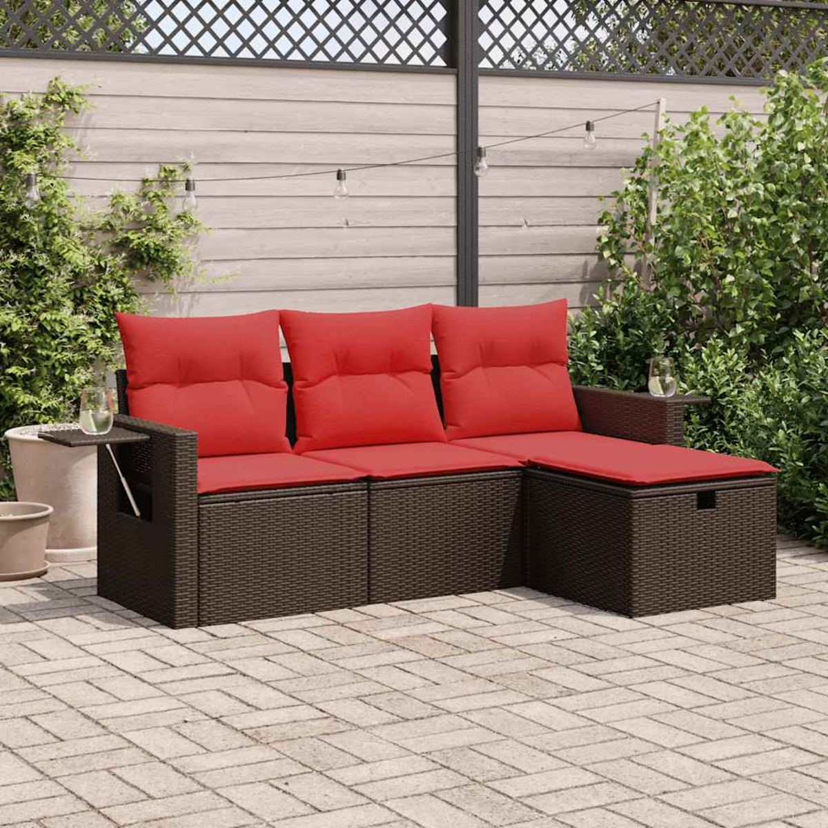 Szene einer Terrasse mit einem braunen Ecksofa aus Korbgeflecht mit roten Kissen. Im Hintergrund Pflanzen.