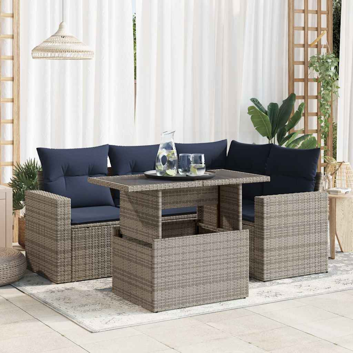 Rattan-Outdoor-Set mit einem anhebbaren Tisch. Zwei Stühle mit blauen Kissen. Weiße Vorhänge und eine Pflanze im Hintergrund.