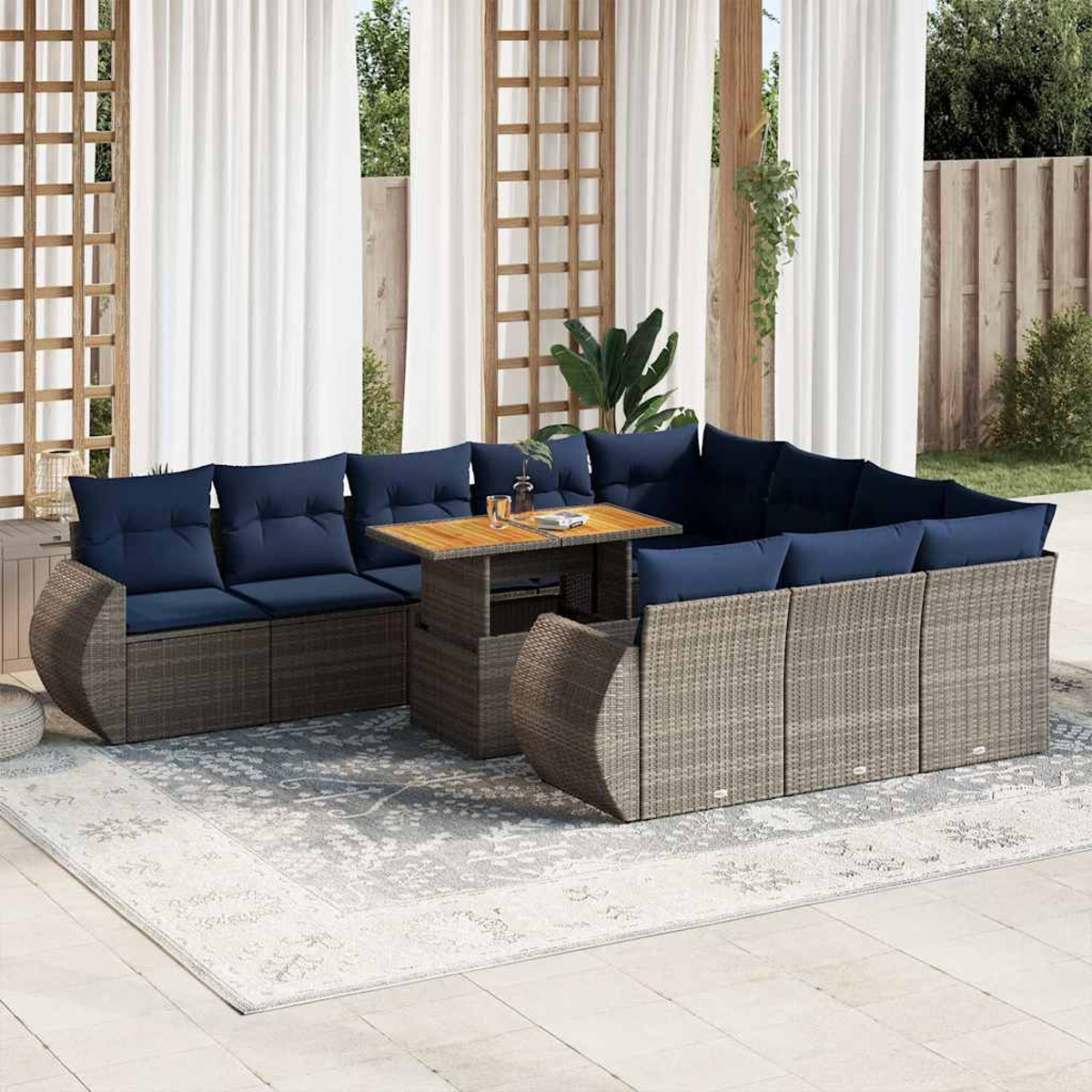 Gartenmöbel-Set auf einem gemusterten Teppich. Das Set umfasst Sofas, einen Tisch und blaue Kissen. Weiße Vorhänge im Hintergrund.