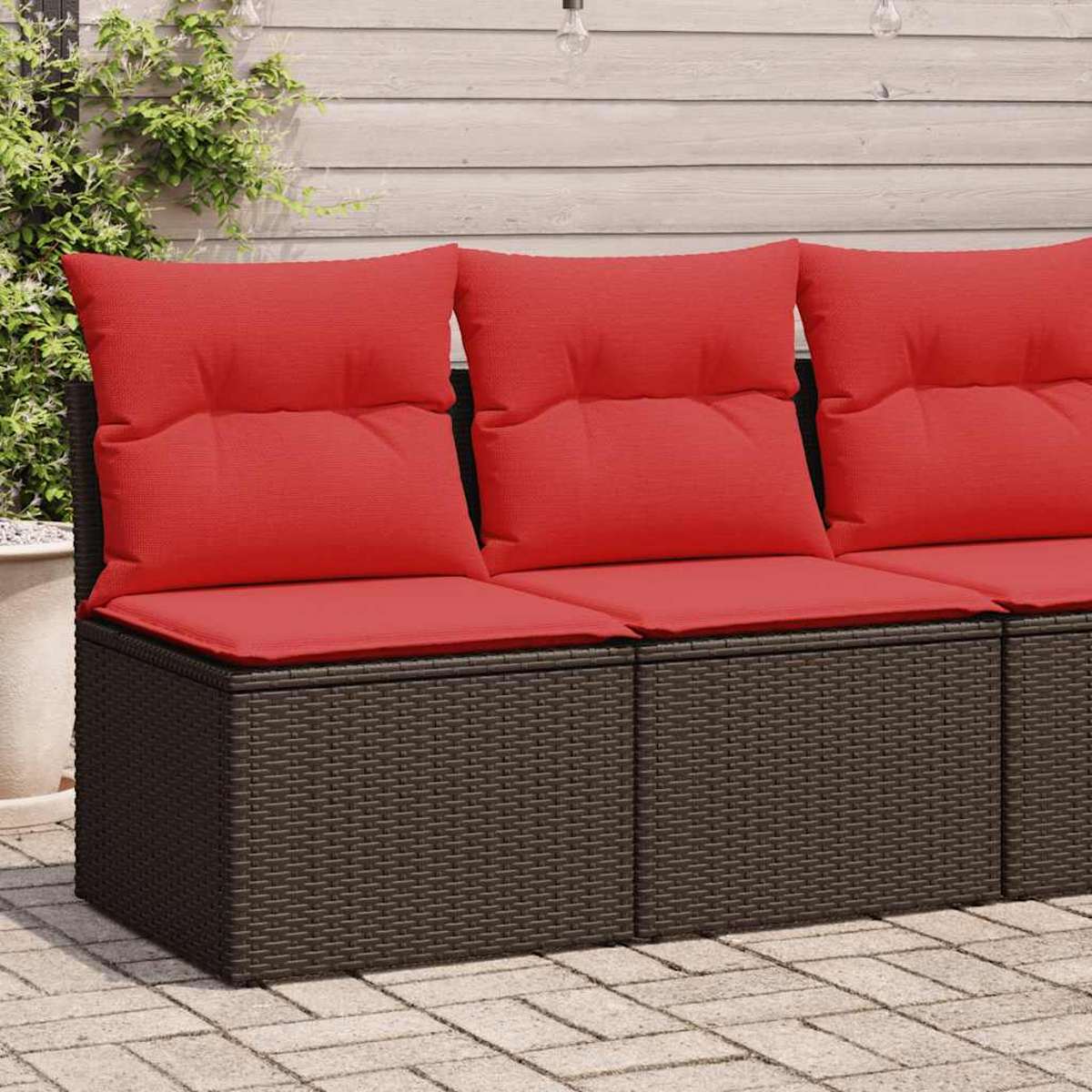 Ein modulares Outdoor-Sofa mit braunem Korbgeflecht und roten Kissen steht auf einer Backsteinterrasse.