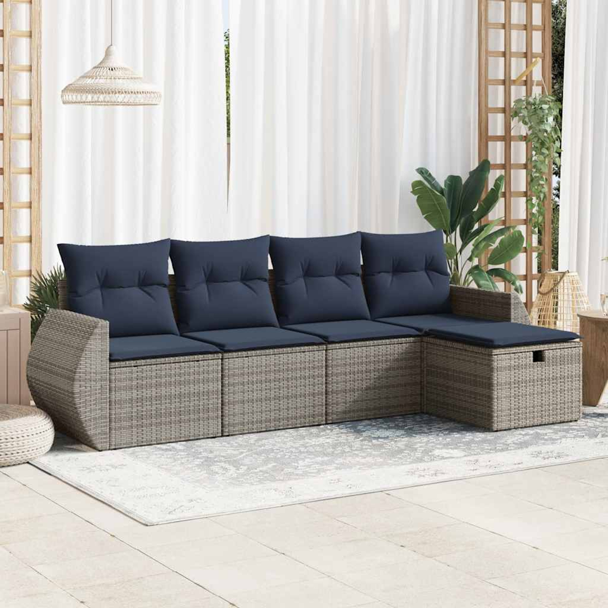 Rattansofa mit blauen Kissen und einem Holztisch auf einem Teppich. Weiße Vorhänge und eine Pflanze.