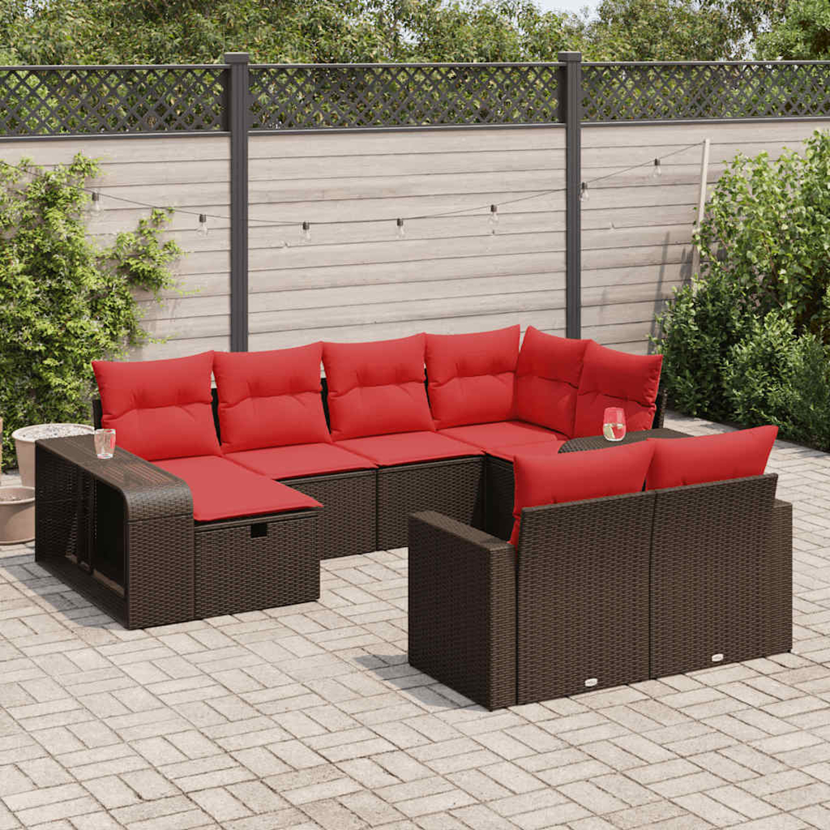 Ecksofa aus Korbgeflecht im Freien mit roten Kissen. Auf einer Backstein-Terrasse mit Zaun im Hintergrund.
