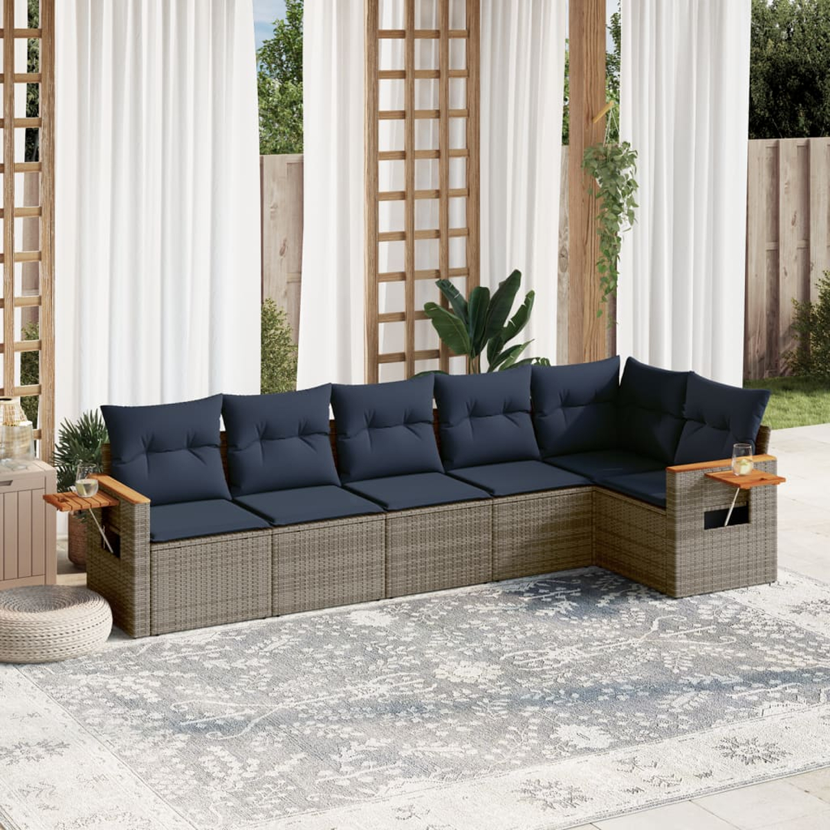 Ein graues Korbssofa mit blauen Kissen, mit Teppich und Vorhängen im Hintergrund. Es ist ein Outdoor-Setup.