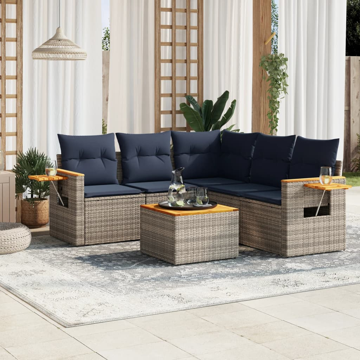 Außenszene mit grauem Rattan-Ecksofa, blauen Kissen, Holztisch und Teppich mit Getränken.