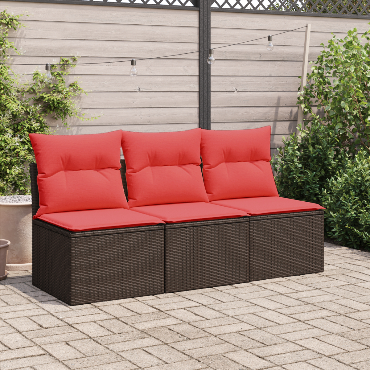 Braunes Outdoor-Wicker-Sofa mit roten Kissen. Die Szene ist eine Terrasse mit Holzzaun und Grün.