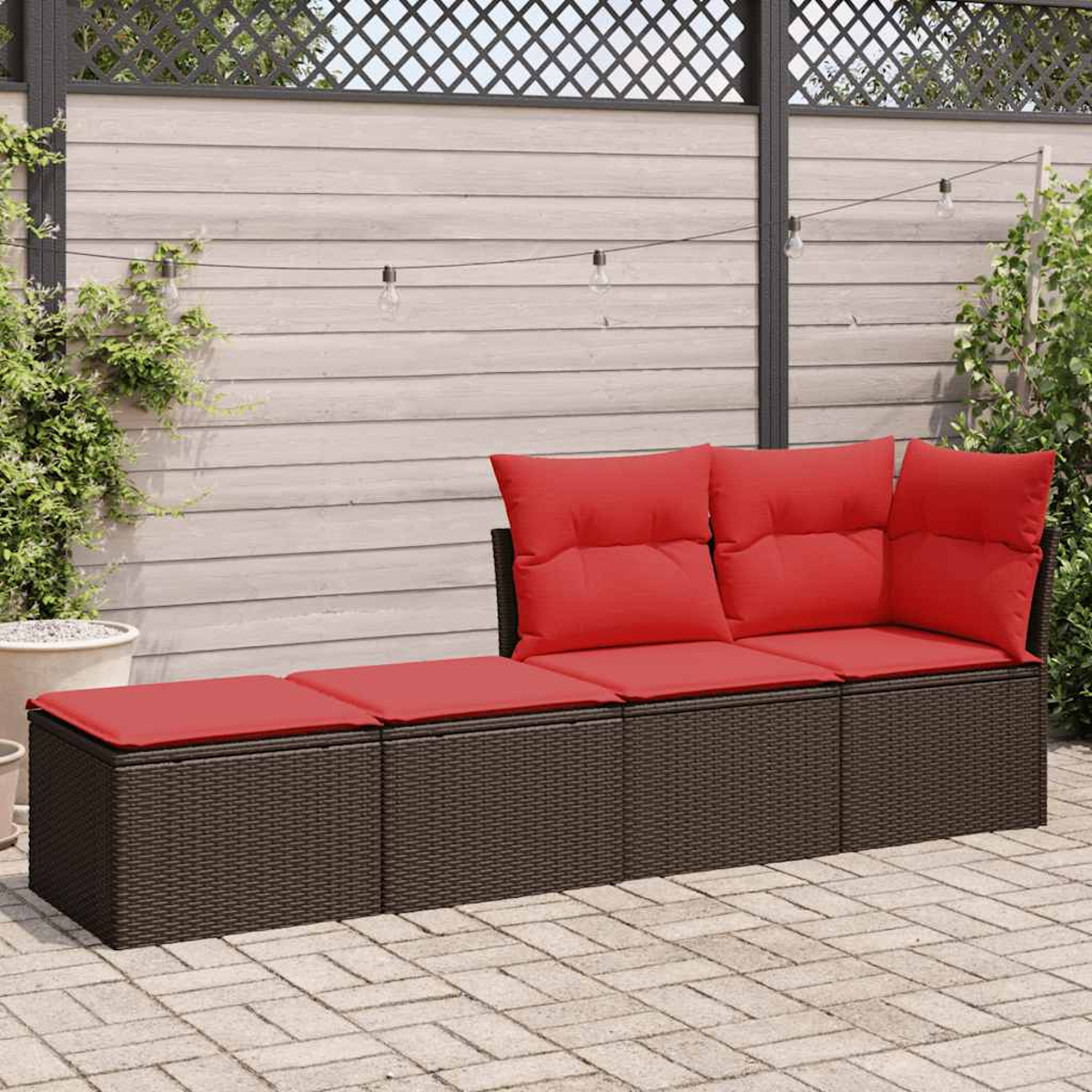 Braunes Outdoor-Korbmöbel mit roten Kissen. Auf einer Ziegelterrasse, mit Holzzaun und Grün im Hintergrund.