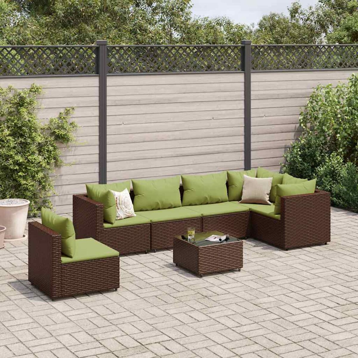 Set da patio in vimini con cuscini verdi su un patio. Include divano componibile e tavolino.