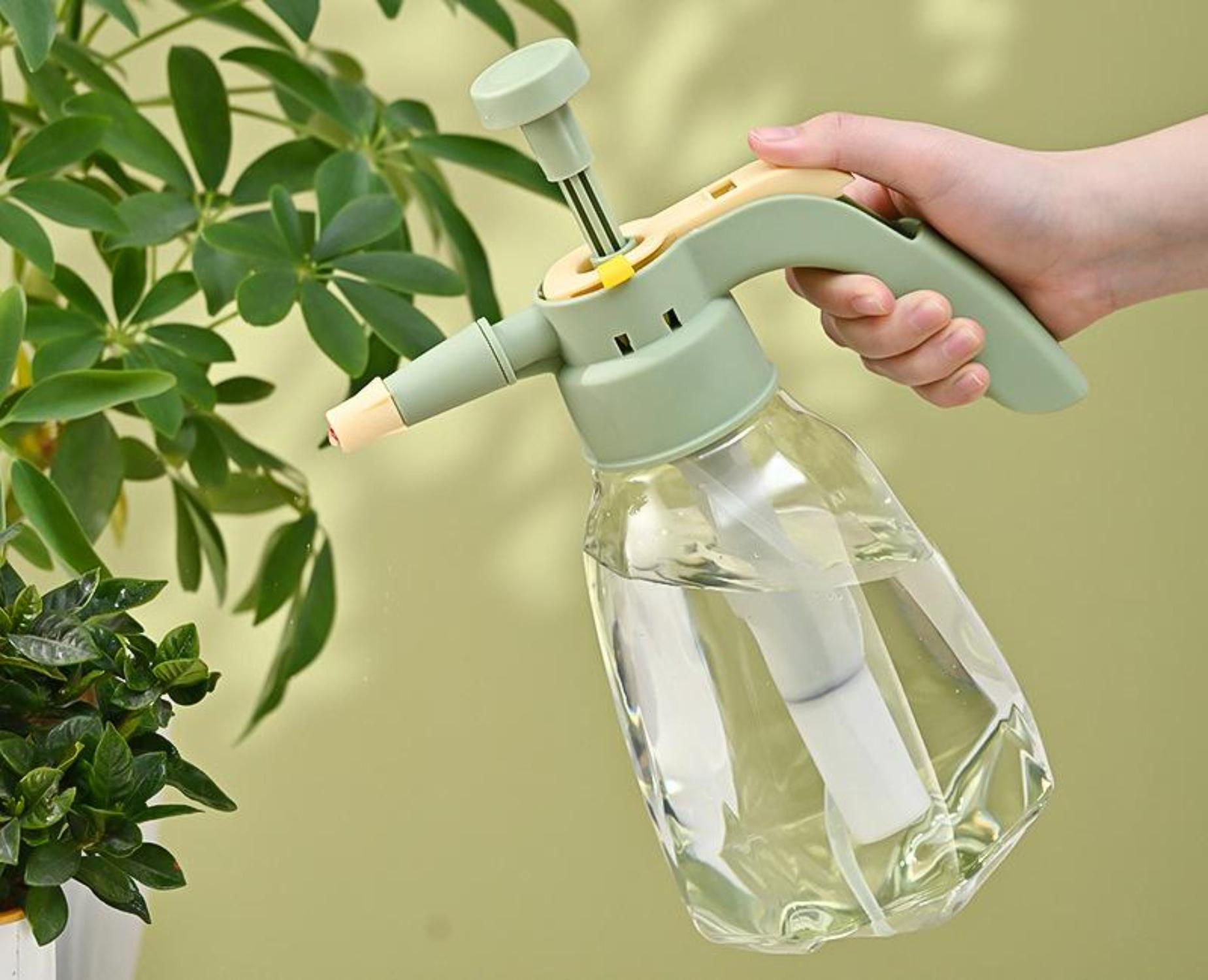 Grüner und klarer Wassersprüher, gehalten von einer Hand. Grüne Pflanze im Hintergrund.