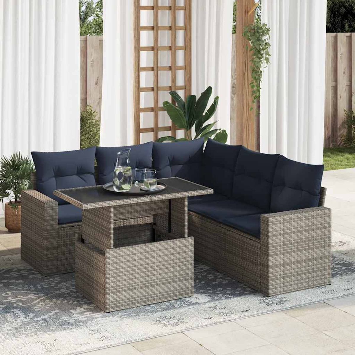 Ein graues Rattan-Patio-Set mit blauen Kissen, Grün und einem weißen Vorhang im Hintergrund.