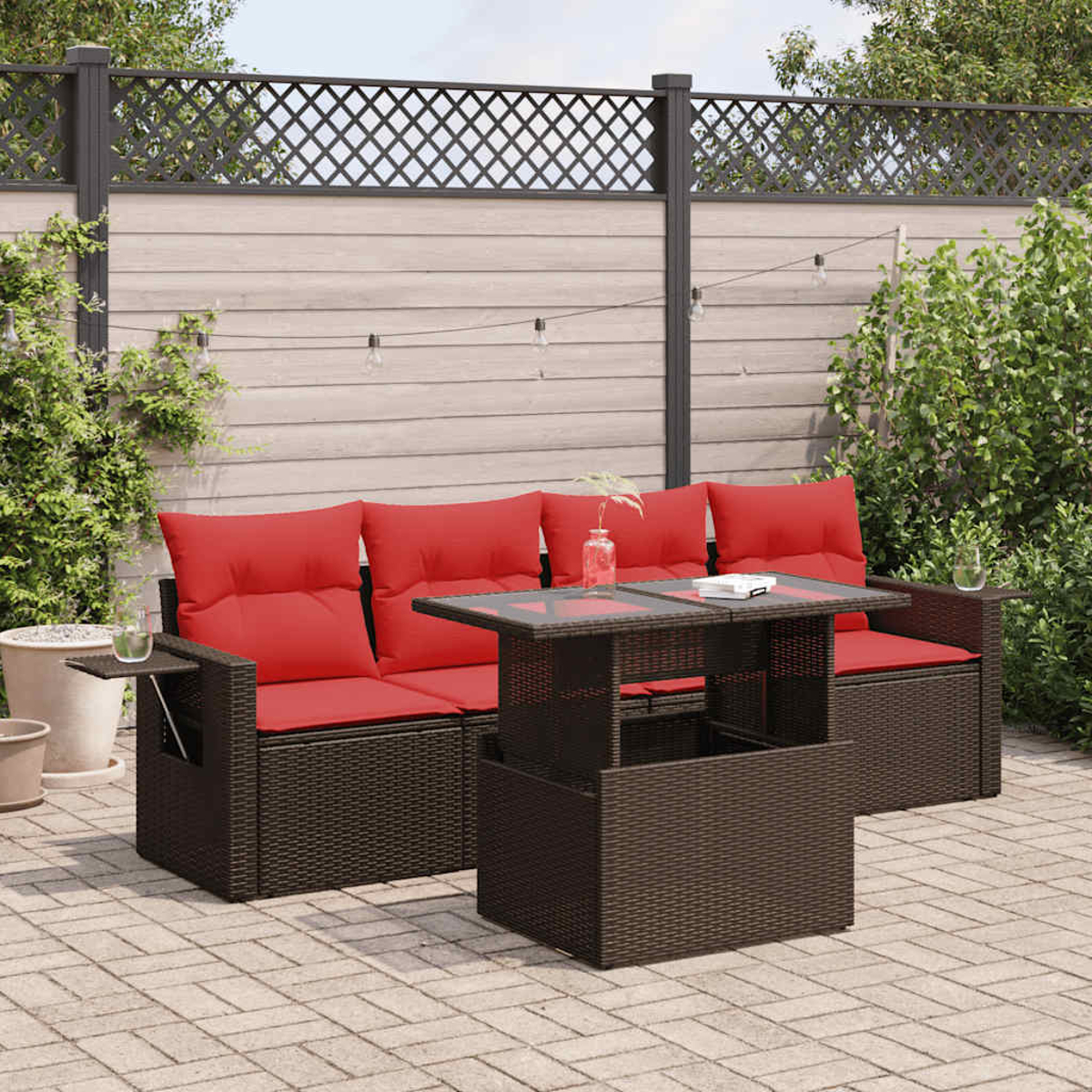 Ein braunes Korbmöbel-Set im Freien mit roten Kissen, einem Tisch und einer Gartenkulisse.