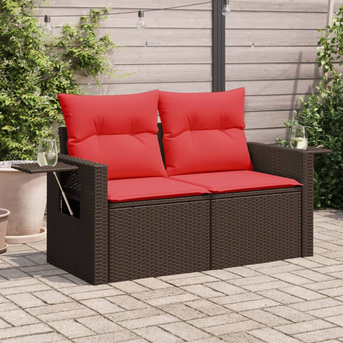 Ein braunes gewebtes Sofa mit roten Kissen und Beistelltischen mit Getränken auf einer Backstein-Terrasse.