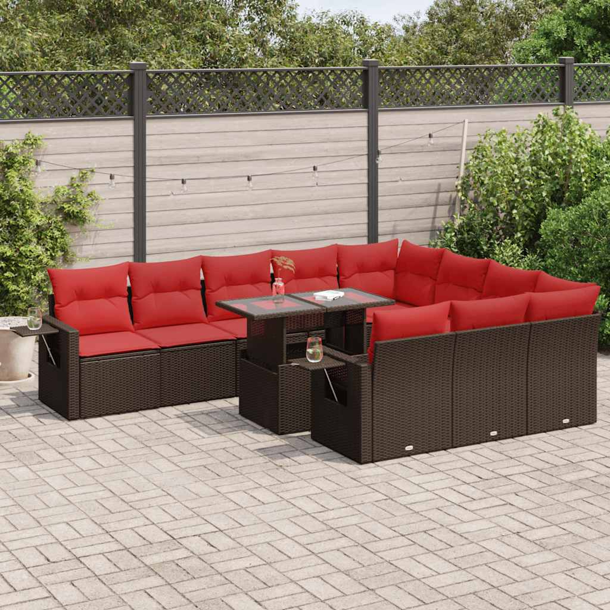 Ein braunes Rattan-Ecksofa mit roten Kissen und einem Tisch auf einer Ziegelterrasse im Freien.
