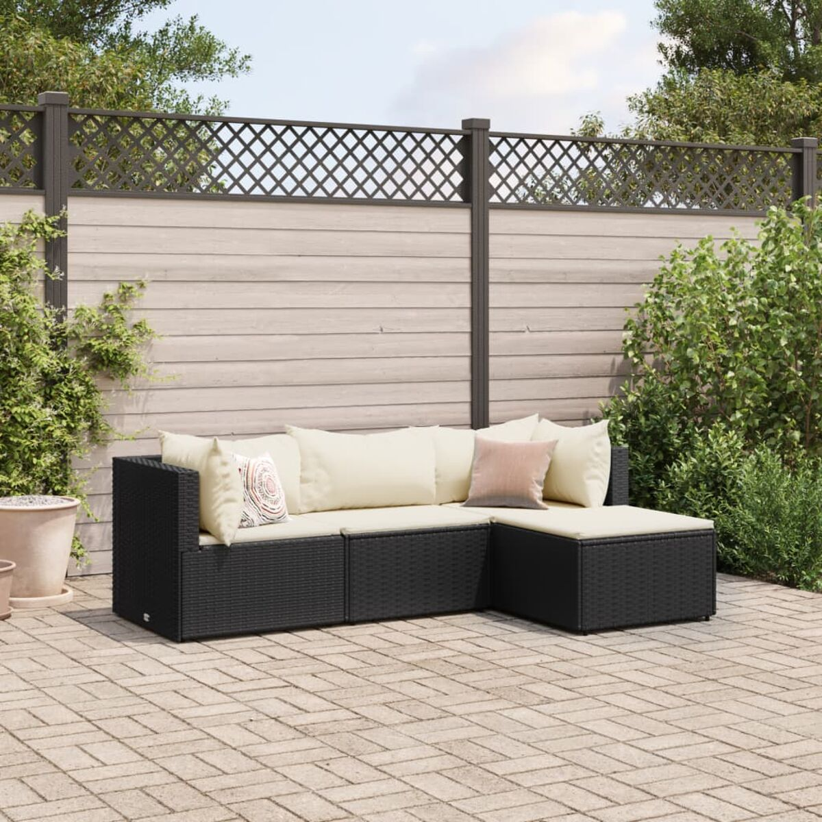 Schwarzes Rattan-Ecksofa mit cremefarbenen Kissen und Zierkissen auf einer Ziegelterrasse mit Pflanzen und Zaun.