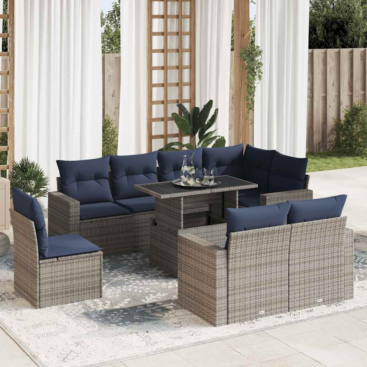 Ein Rattan-Terrassenset mit marineblauen Kissen. Es beinhaltet ein Sofa, Stühle und einen Tisch, auf einem Teppich, mit Vorhängen.