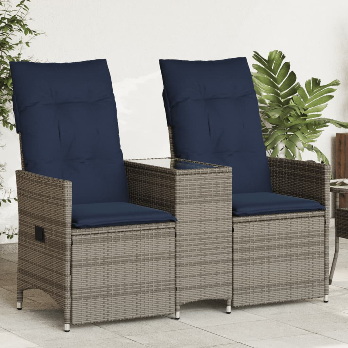 Zwei graue Rattan-Stühle mit marineblauen Kissen und einem kleinen Tisch dazwischen, in einer Gartenumgebung.