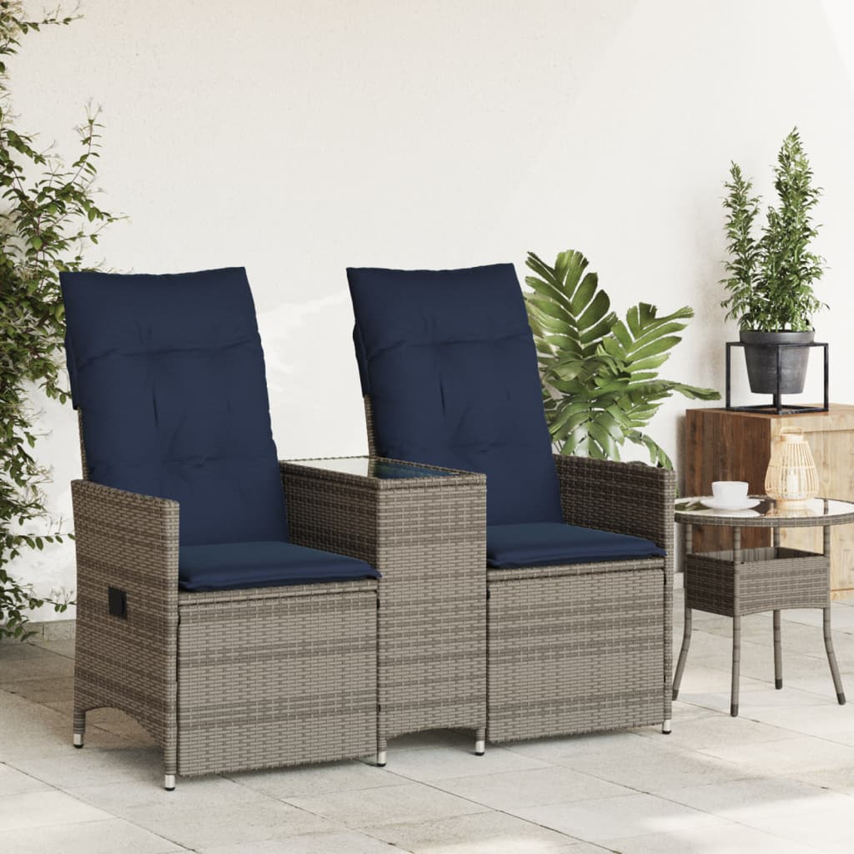Zwei graue Rattan-Stühle mit marineblauen Kissen und einem kleinen Tisch dazwischen, auf einer Terrasse mit einer Pflanze.