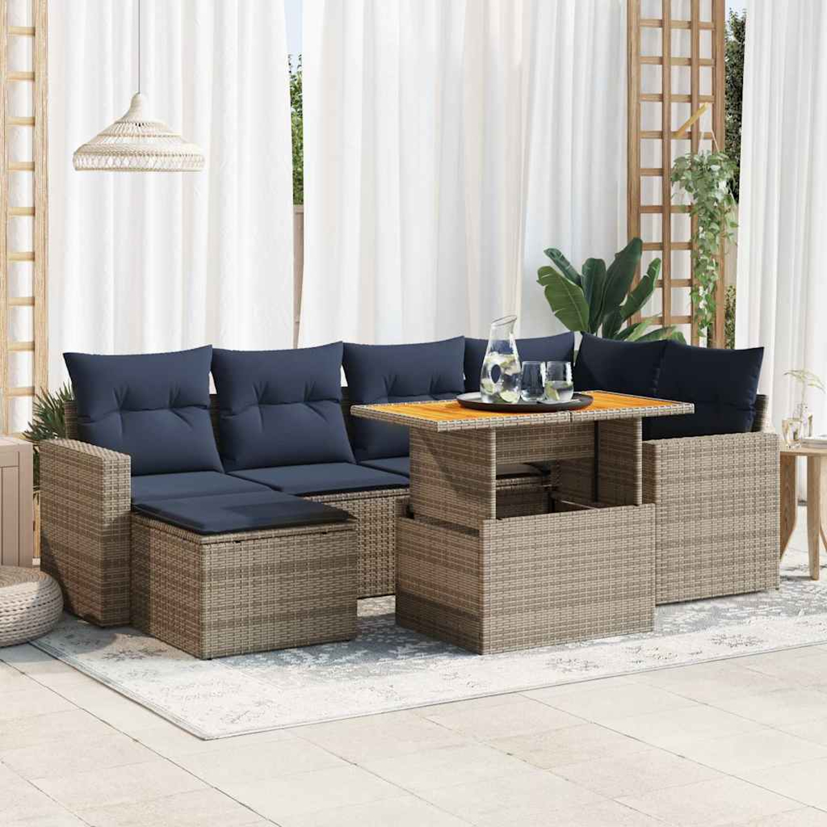 Outdoor-Rattan-Sofagarnitur mit marinefarbenen Kissen, einem aufsteigenden Tisch mit Holzplatte und weißen Vorhängen im Hintergrund.