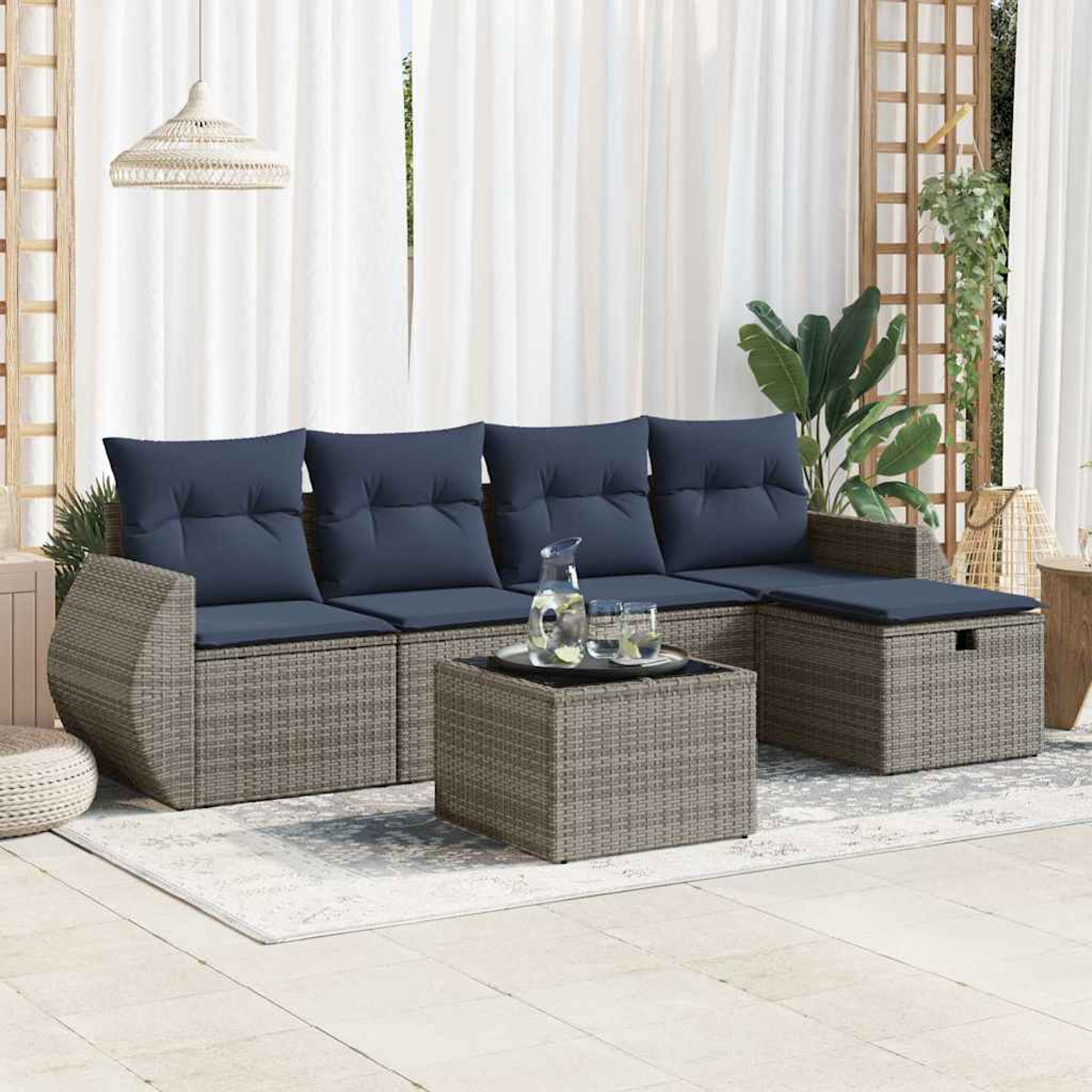 Ein Outdoor-Sofaset mit blauen Kissen, einem Glas Wasser und einem Tisch mit Teppich.