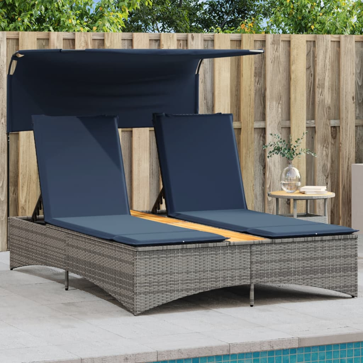 Due chaise longue da esterno con cuscini blu e tenda da sole, accanto a una staccionata in legno e un tavolino.