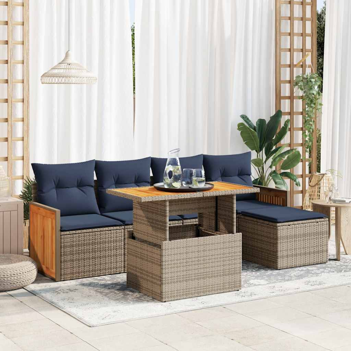 Ein graues Korbmöbel-Set mit marineblauen Kissen und einem Holztisch. Es gibt einen Teppich, eine Pflanze und weiße Vorhänge.
