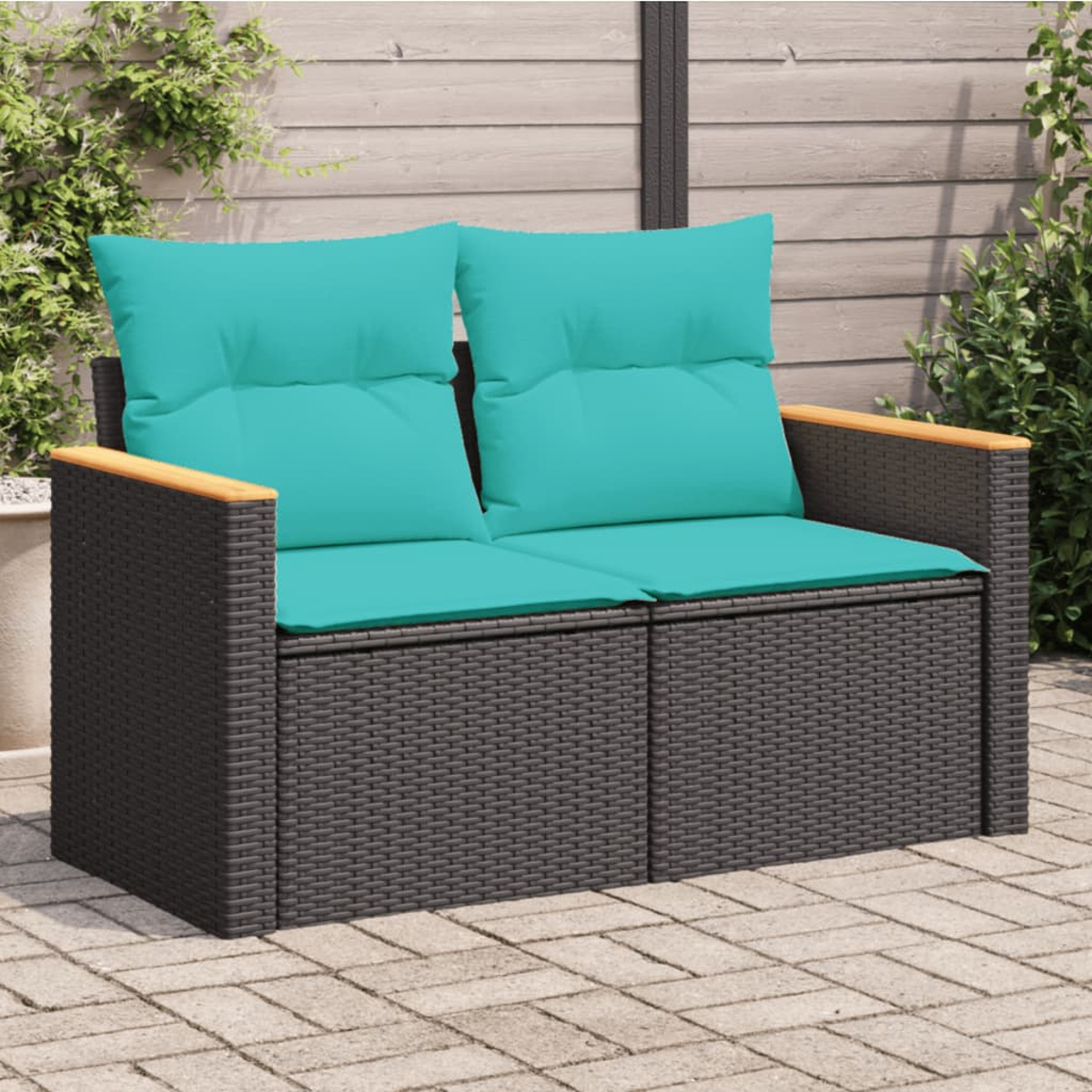 Ein Zweisitzer-Wicker-Sofa mit tealfarbenen Kissen und Holzarmlehnen auf Ziegelpflaster.